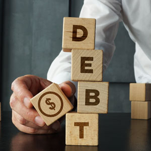 hand stacks wooden blocks spelling “DEBT” with a dollar sign block