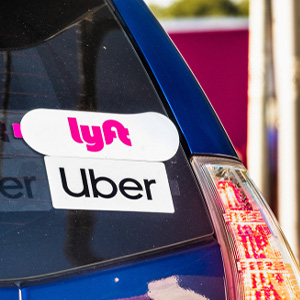 Uber and Lyft stickers on a car rear window, discussing bankruptcy effects on Florida rideshare drivers with car loans/leases.